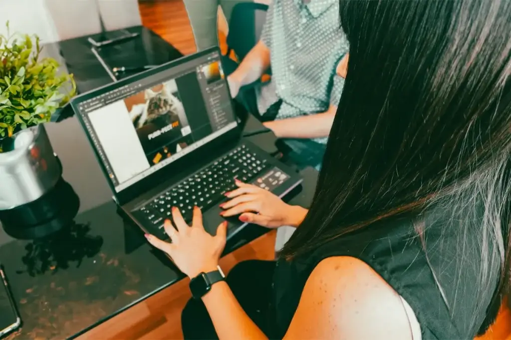 A female graphic designer working on Adobe Illustrator with a blurred background with her peers next to her