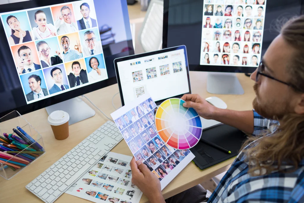 male executive working at his desk looking at different images of people on his screen while holding a color wheel to ensure visual colour cohesion